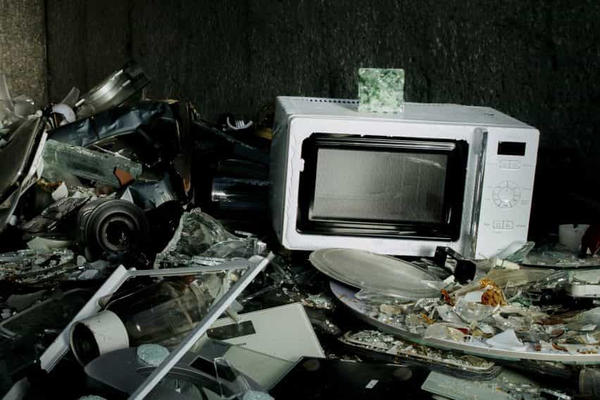 Una baldosa de Common Sands sentada encima de un microondas en una pila de vidrio roto y desechos electrónicos