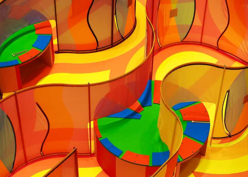 Dos xilófonos circulares grandes y coloridos incrustados dentro de paredes de laberinto de malla ondulada en la instalación Listening to Joy