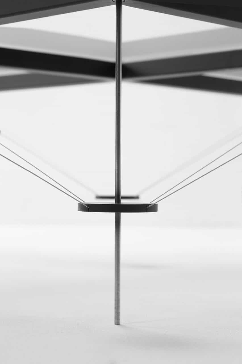 Primer plano en TT_01 mesa que muestra delgadas patas de metal con discos de acero a mitad de camino sosteniendo cables de tensión en su lugar que llegan hacia una gruesa estructura metálica en la parte superior