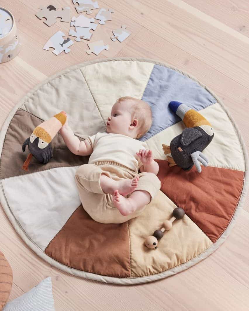 Foto de un bebé en una alfombra de juego OYOY Living Design estampada con una rueda de colores de tonos terrosos y pasteles apagados jugando con peluches de punto