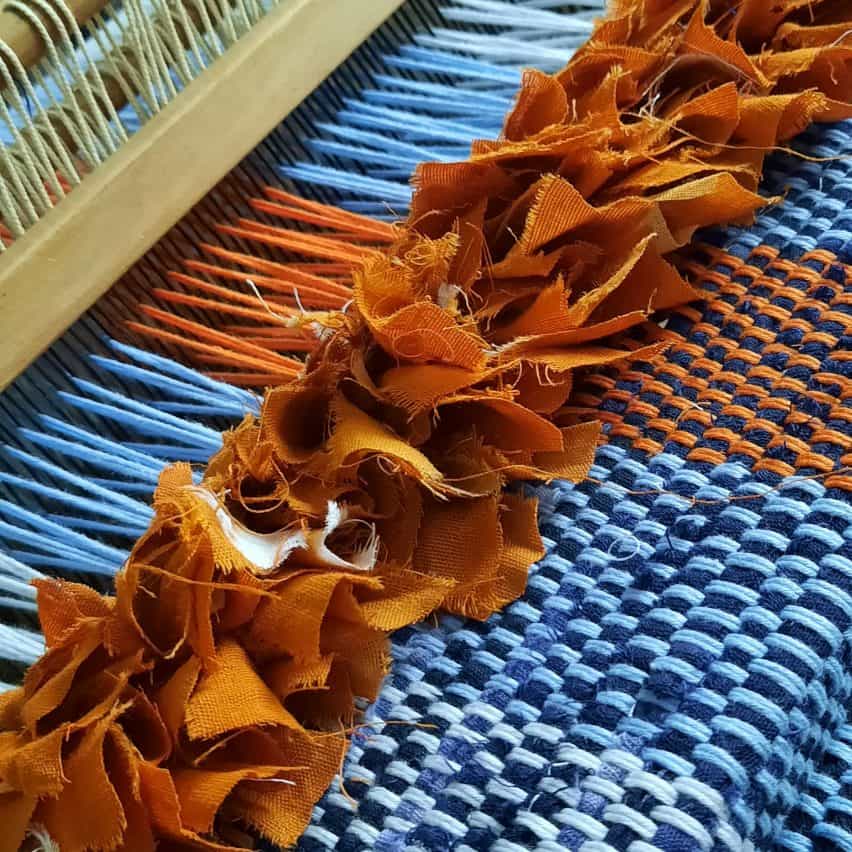 Primer plano del proceso de tejido de tela Dakala por Nkwo Onwuka con hilo azul y naranja