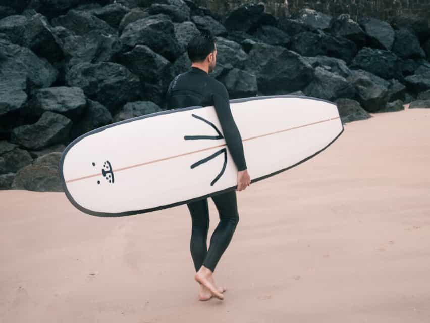 Un surfista lleva la tabla de surf de foca a través de una playa.