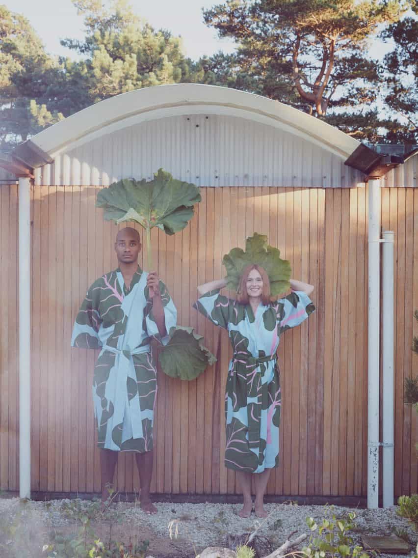 Dos personas con albornoces azules y verdes sosteniendo hojas grandes