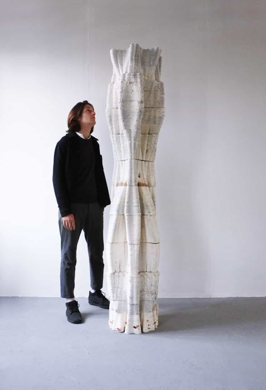 Hombre de pie junto a una columna de árbol impresa en 3D de micelio que se eleva sobre él